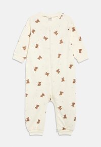 Krēmkrāsas zīdaiņa kombinezons ar brūna tēja lāča, zvaigznes un pusmēness rakstu, garām piedurknēm un rāvējslēdzēju priekšpusē.