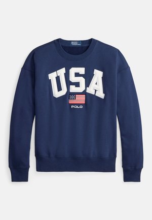 Sötétkék pulóver „USA” fehér betűkkel, kis amerikai zászlóval és „POLO” felirattal alatta. Bordás szegélyek az ujj- és derékrészen. Puha pamut keverék.