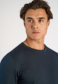 Tumma laivansiniset pitkähihainen paita, jossa on pyöreä pääntie. Suora pinta, vartalonmyötäinen muotoilu, yksinkertainen rakenne ilman kuvioita tai koristeita.