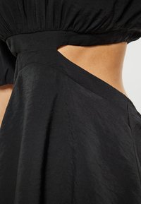 Schwarzes Kleid mit einem taillierten Oberteil und einem Ausschnitt sowie einem fließenden, strukturierten Rock. Der Stoff hat eine leicht zerknitterte Oberfläche.