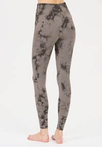Leggings grises con un patrón de mármol negro, fabricados con material elástico. Cuentan con una cinturilla alta y un pequeño logotipo en la parte posterior.