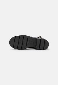 Semelle de chaussure en caoutchouc noir avec des rainures de traction profondes et un logo en relief. Présente un design plat et une surface texturée.