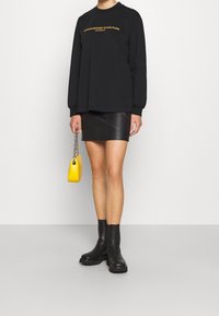 Czarna bluza z długim rękawem z żółtym napisem, w połączeniu z czarną skórzaną mini spódnicą, czarnymi botkami na kostkę oraz małą żółtą torebką.