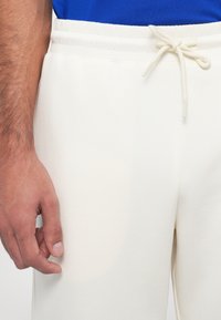 Pantalon de jogging beige clair avec une taille élastique et un cordon de serrage, présentant une texture lisse et sans motifs ni accents visibles.