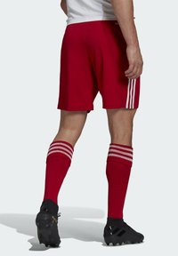 Red athletic shorts with three white stripes on the sides, paired with red socks featuring white stripes, and black football cleats.