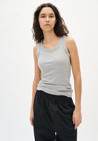 Pilkas banguotas tanktopas su apvaliu iškirpimu, derinamas su juodomis laisvomis kelnėmis. Audinys yra minkštas, sukuriantis kasdienę išvaizdą.