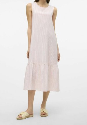 Vrouw draagt een mouwloze, lichtroze midijurk met subtiele verticale strepen en een gerafelde zoom, gecombineerd met beige instapsandalen.