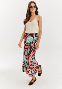 Maxi sukňa s kvetinovým vzorom v odvážnych odtieňoch ružovej, tyrkysovej a hnedej, v kombinácii s krémovým topom a hnedými topánkami, s tenkými ramienkami.