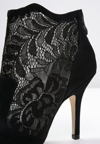 Stivale nero alla caviglia dal design elegante, con pannello in rete di pizzo e materiale scamosciato. Il tacco è di tipo stiletto, aggiungendo altezza.