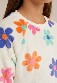 Vitt fleece-sweatshirt med flerfärgade blommor i lila, orange, rosa och turkos. Rundad halsringning med ribbade detaljer.
