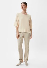 Jasno beżowy sweter z okrągłym dekoltem i krótkimi rękawami, w połączeniu z jasno beżowymi spodniami i meshowymi czółenkami z ostrym noskiem.