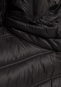 Close-up van zwart doorgestikt textiel met stikseldetails en een gedeeltelijk gesloten zwarte ritssluiting op glanzend materiaal.