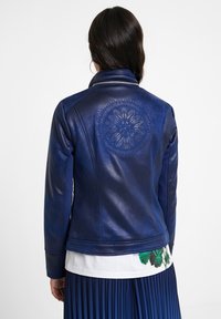 Granatowa skórzana kurtka o dopasowanym fasonie z ozdobnym haftem na plecach. Posiada standardowy kołnierz i smukłą sylwetkę.