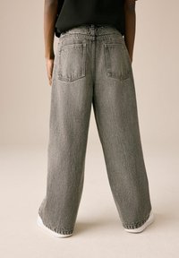 High-waisted wide-leg jeans in gray denim, featuring two back pockets, minimal stitching, and a slightly frayed hem. Paired with white sneakers.
