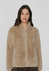 Chaqueta de felpa beige con cremallera y cuello alto, de mangas largas, hecha de un material sintético suave, con un corte holgado.