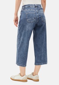 Culottes de denim azul con rayas blancas verticales, dos bolsillos traseros y un diseño recortado. Combinados con zapatillas blancas.