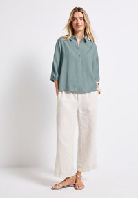 Camicia azzurra chiaro con un design a bottoni e maniche arrotolate, abbinata a pantaloni larghi in lino off-white e sandali con cinturini.