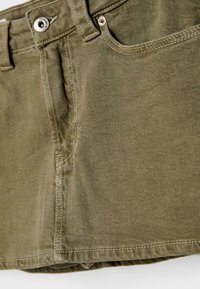 Gonna di jeans verde oliva con tasca frontale, passanti per cintura e chiusura a bottone in metallo. La texture è liscia con dettagli di cucitura visibili.