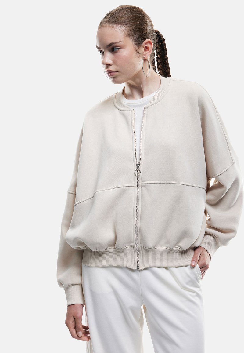 Overdimensioneret beige sweatshirt med rund halsudskæring, frontlynlås og ribstrikkede manchetter. Blødt stof med en glat overflade og afslappet pasform.