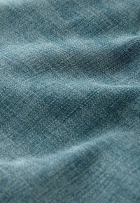 Gros plan d’un tissu denim bleu texturé avec des fibres tissées visibles et des plis subtils créant des motifs ondulés.
