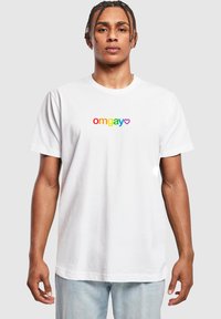 Hvid bomulds t-shirt med "omgay" tekst i regnbuens farver og et hjerteaccent. Korte ærmer og afslappet pasform. Glat tekstur.