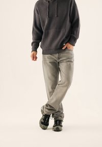 Grau gestreifter Hoodie mit einer Tasche, kombiniert mit hellgrauen Jeans und schwarzen Sneakers. Das Outfit zeichnet sich durch einen lockeren Schnitt und strukturierte Materialien aus.