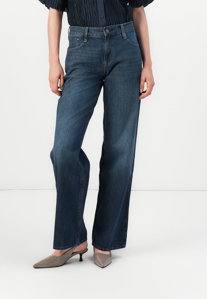 Donkerblauwe, wijde spijkerbroek van denim met een hoge taille, voorzien van voorzakken en een ritssluiting. Gladde textuur, minimale detailing.