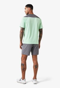 Camiseta deportiva de manga corta en verde claro con detalles grises, combinada con pantalones cortos grises. Presenta una textura transpirable y un ajuste cómodo.
