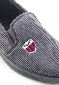 Scarpa slip-on in corduroy grigio con suola in gomma nera e logo scudetto ricamato in accenti rossi e blu. Tessuto morbido e design casual.