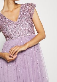 Levandulové šaty s výstřihem do V a krátkými volánovými rukávy, zdobené flitry, s plisovanou sukní a jemnou, průhlednou texturou.