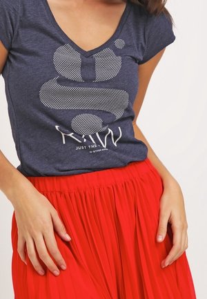 Mørkeblå V-hals t-shirt med hvidt prikket motiv og tekst, kombineret med en rød plisseret nederdel, der viser blødt stof og en afslappet pasform.