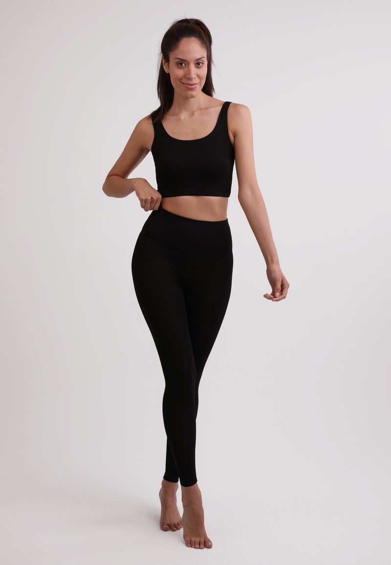 Top corto nero e leggings a vita alta realizzati in tessuto elasticizzato. Entrambi i capi presentano una texture liscia e un design aderente.