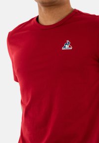 Camiseta de algodón roja con cuello redondo y mangas cortas, con un pequeño logotipo bordado en la parte izquierda del pecho.