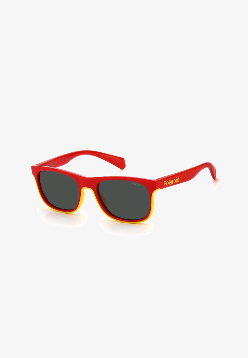 Lunettes de soleil rouges avec des accents jaunes, verres carrés et une monture en plastique brillant. Présente le logo de la marque sur la branche.