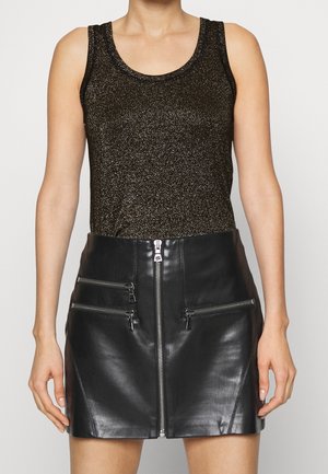 Kvinde iført en sort glitrende ærmeløs top og en sort læderminiskirt med lynlås foran og to lynlåslommer.