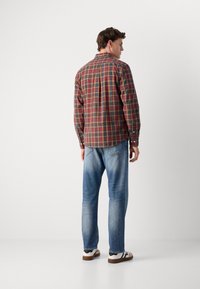 Lange mouwen geruite blouse met rode, groene en gele ruiten, knoopmanchetten en een afgeronde zoom, gecombineerd met lichtblauwe jeans en casual schoenen.