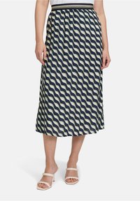 Jupe midi à motifs avec un design ondulé bleu marine et crème, taille élastique, tissu léger, associée à des sandales à talons beiges.