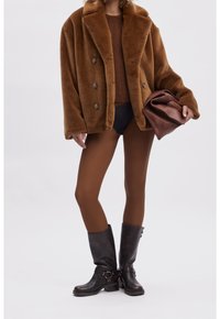 Brun faux fur dubbelknäppt jacka, texturerad stickad topp, svarta stövlar, bruna strumpbyxor och en brun clutch-väska.