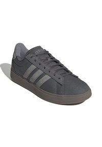 Sneaker Adidas grigio scuro a bassa altezza con suola in schiuma, allacciatura frontale e tre strisce grigio più chiare sul lato.