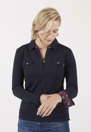 Polo à manches longues bleu marine avec deux poches poitrine, boutons dorés et poignets à motif floral. Tissu doux avec un col et une coupe décontractée.