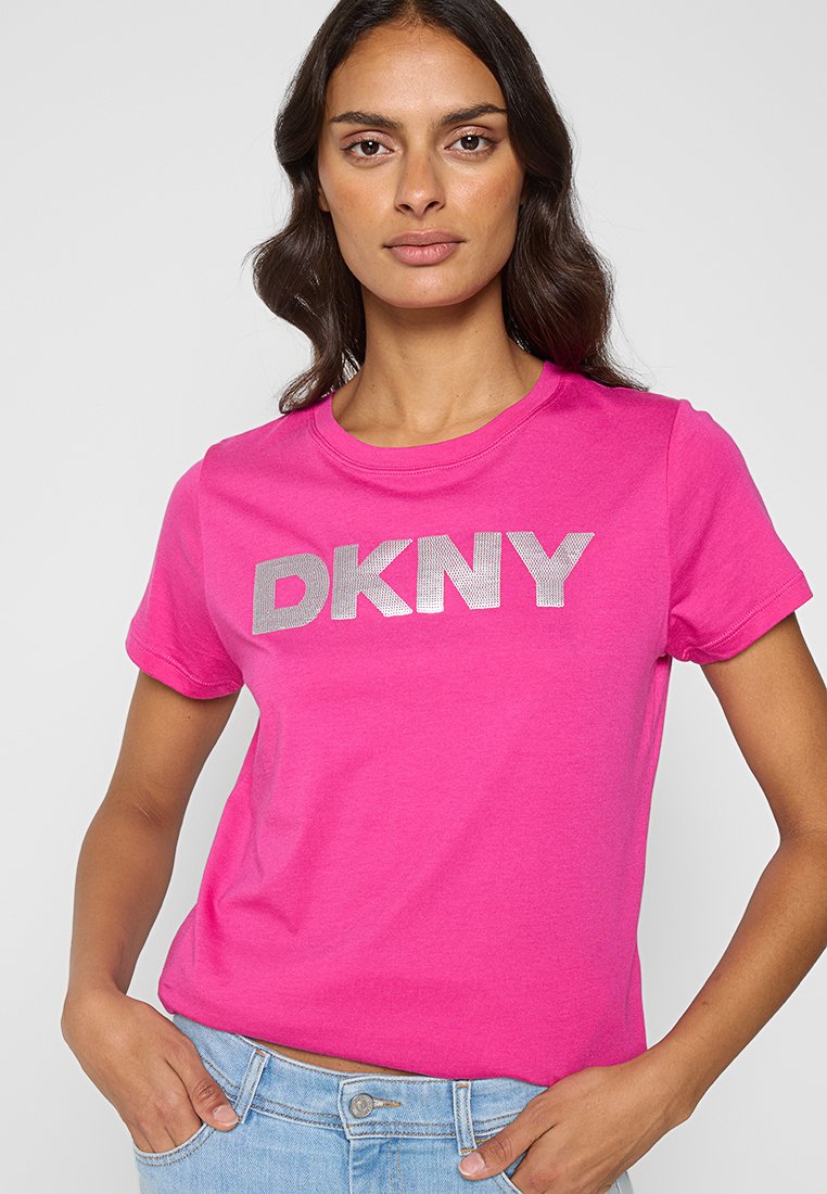 Fuksjowa bawełniana koszulka z krótkim rękawem z klasycznym okrągłym dekoltem, z srebrnym logo DKNY. Krój jest luźny i casualowy.