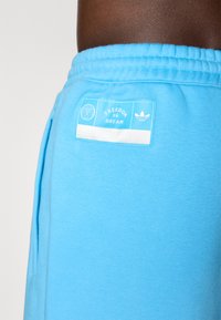 Light blue athletic shorts made of soft fabric, featuring a white label with "FREEDOM TO DREAM" and the Adidas logo on the pocket area.
