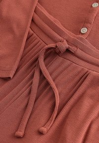 Rust-colored dress featuring a ribbed texture, button closure, and a tied waist. The fabric appears soft and lightweight.