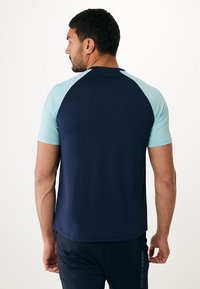 Námořnické sportovní tričko s krátkým rukávem a světle modrými raglánovými rukávy; vyrobeno z lehkého, pružného materiálu; má kulatý výstřih.