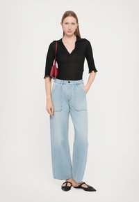 Black, fitted crop top with short, frayed sleeves; light blue, wide-leg jeans; black, flat-heeled shoes; small red handbag.