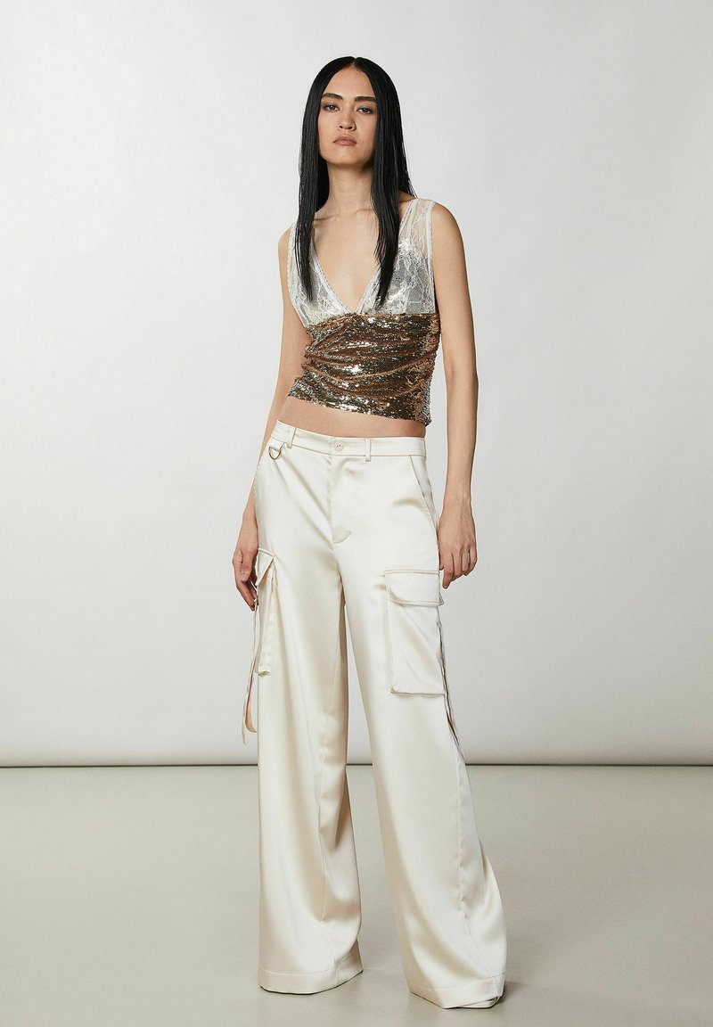 Metaliczna srebrna i brązowa bluzka ze cekinami z dekoltem w kształcie litery V; wysokie, kremowe satynowe spodnie cargo z kieszeniami i bocznymi akcentami.