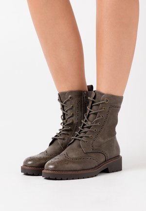 Olivgrüne Leder-Stiefeletten mit Broguedetails, Schnürung vorne und seitlichem Reißverschluss. Klobige braune Sohle mit strukturiertem Profil.
