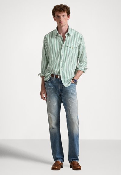 Πουκάμισο με ανοιχτοπράσινες και λευκές ρίγες, κουμπωμένο με τσέπη στο στήθος. Φορεμένο με ξεβαμμένο μπλε τζιν με πιτσιλιές μπογιάς, συμπληρωμένο με καφέ παπούτσια.