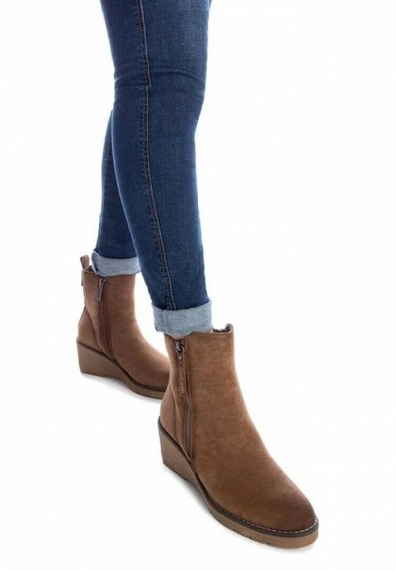 Personne portant un jean skinny bleu retroussé et des bottines compensées en daim marron avec des zips latéraux.