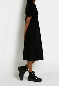 Svart midiklänning i bomull med korta volangärmar, kombinerad med kraftiga svarta snörstövlar med gulddetaljer och textur.